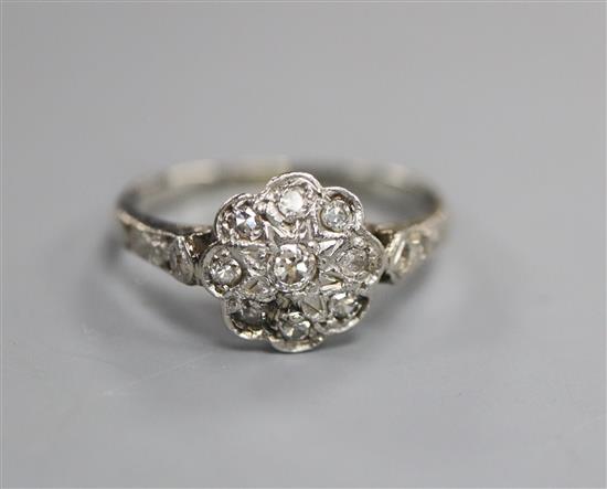 A 1920s white metal and diamond set flower head cluster ring, with diamond set shoulders, size H/I.